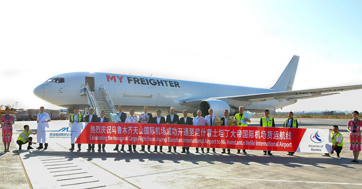 Officials and partners stand on the airport runway in front of a My Freighter cargo aircraft, holding a banner celebrating the inaugural cargo flight between Urumqi Tianshan International Airport and Niš Constantine the Great Airport.