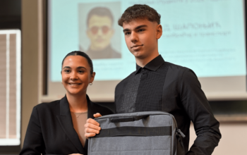 Transfera representative presenting an Excellence Award to a top Logistics student at the Faculty of Transport and Traffic Engineering, with the student holding a laptop bag during the award ceremony.